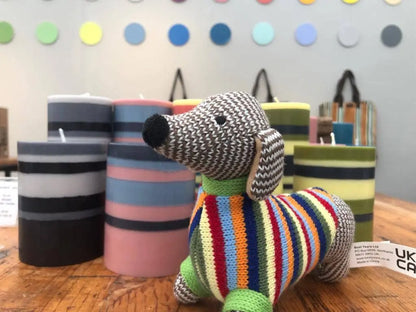 Knitted dog toy in front of striped candles and a polka dot wall.