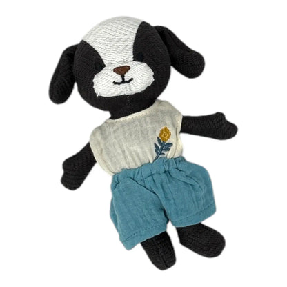 A handmade black and white knitted dog toy wearing a cream-coloured top with a small yellow and blue flower embroidery and teal-blue shorts, isolated on a white background.