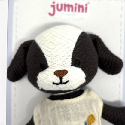A close-up of a handmade knitted dog plush toy by Jumini, featuring a black and white face, a brown embroidered nose, and a cream-coloured sweater with a small yellow flower.