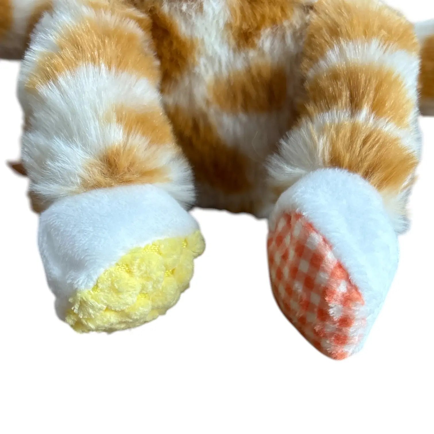 Close-up of a plush toy's front paws and feet, featuring orange and white striped fluffy fur, white padded paw cuffs, one yellow-padded paw cuff, and an orange-and-white checkered paw pad.