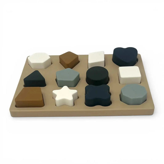 For The Baby silicone shape puzzle with 12 pieces in various shapes and muted colours on a beige board.