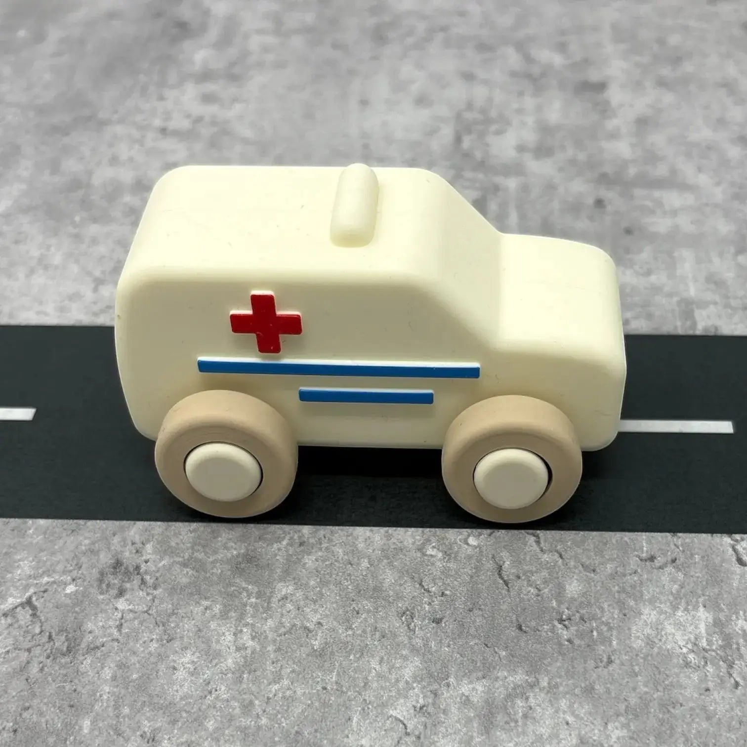 For The Baby cream silicone toy ambulance with red cross and blue stripes, on a grey road surface.
