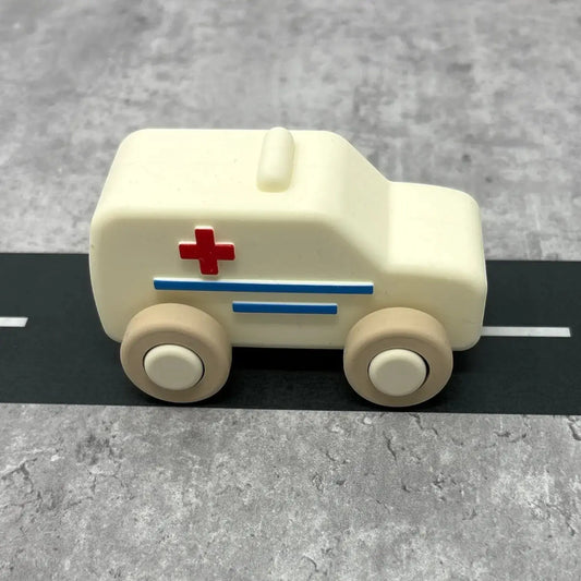 For The Baby cream silicone toy ambulance with red cross and blue stripes, on a grey road surface.