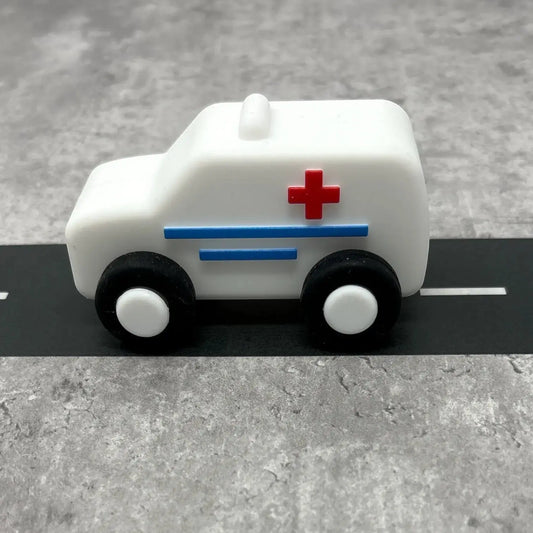 For The Baby white silicone toy ambulance with red cross and blue stripes, on a road.