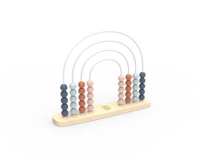 A wooden abacus with five vertical columns of round beads in muted blue, peach, and terracotta tones, suspended by thin white arches on a light natural wood base. A small circular logo is visible in the center of the base.