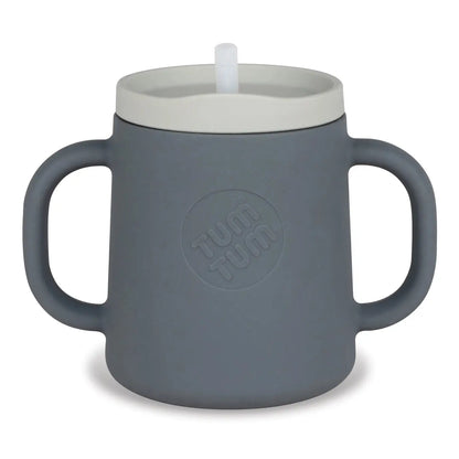 A dark grey silicone baby tumbler with integrated side handles, a light grey lid, and a white straw, featuring an embossed circular 'TUM TUM' logo on the front.