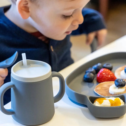 Child with a cup and tray of food on a table