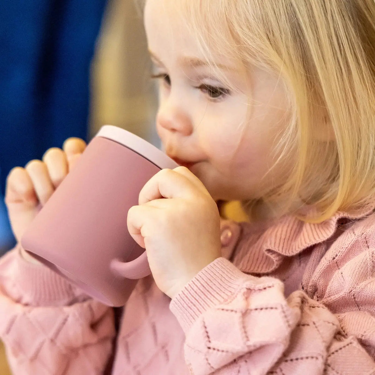 Child drinking from a pink cup with a blurred background
