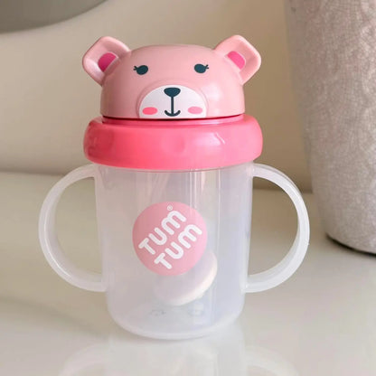 A clear plastic baby tumbler with white handles and a pink bear-shaped lid. The lid features a pink bear face with black eyes and nose, and a pink band around the neck.
