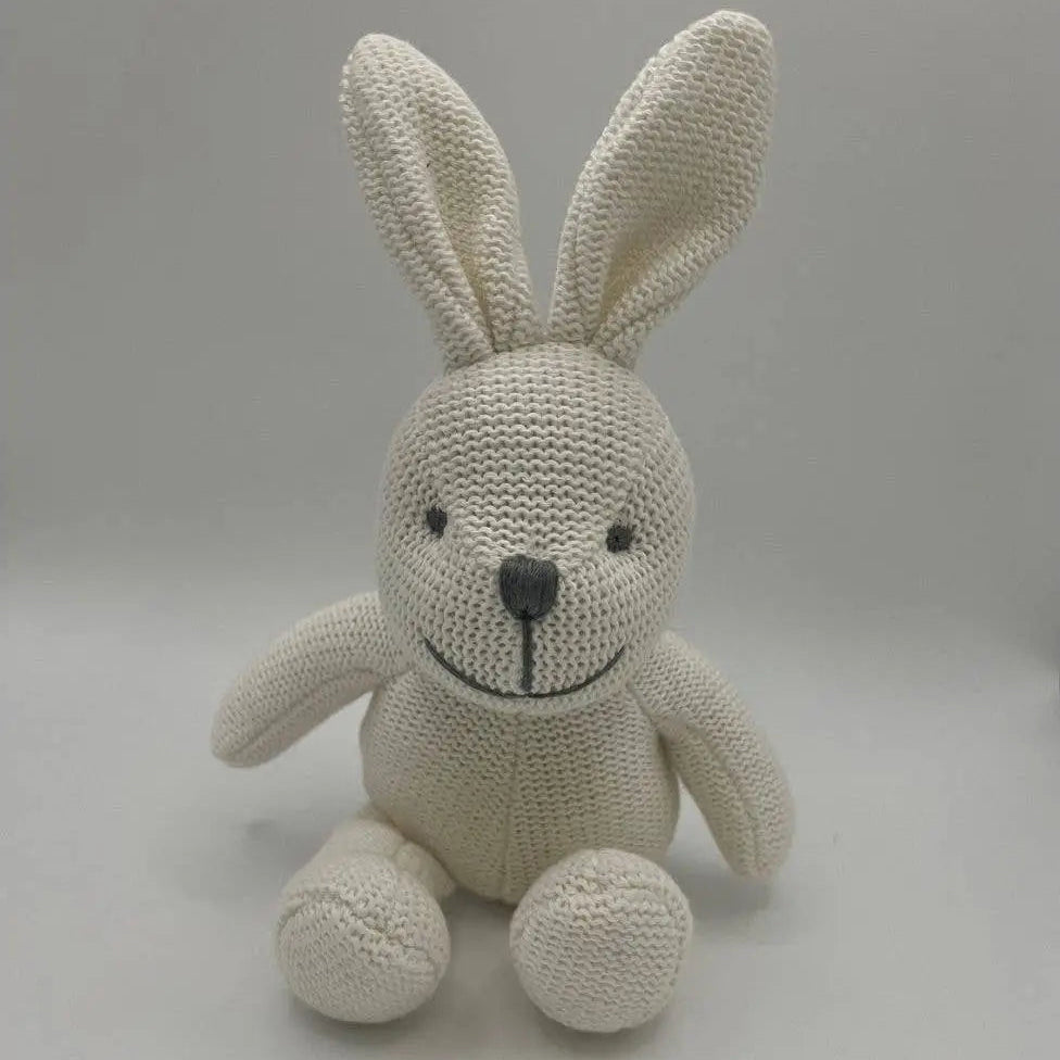 A cream-coloured knitted bunny plush toy with a black embroidered nose and eyes, sitting against a neutral grey background.