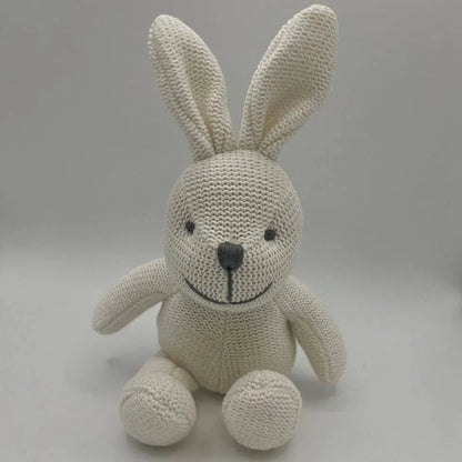 A cream-coloured knitted bunny plush toy with a black embroidered nose and eyes, sitting against a neutral grey background.