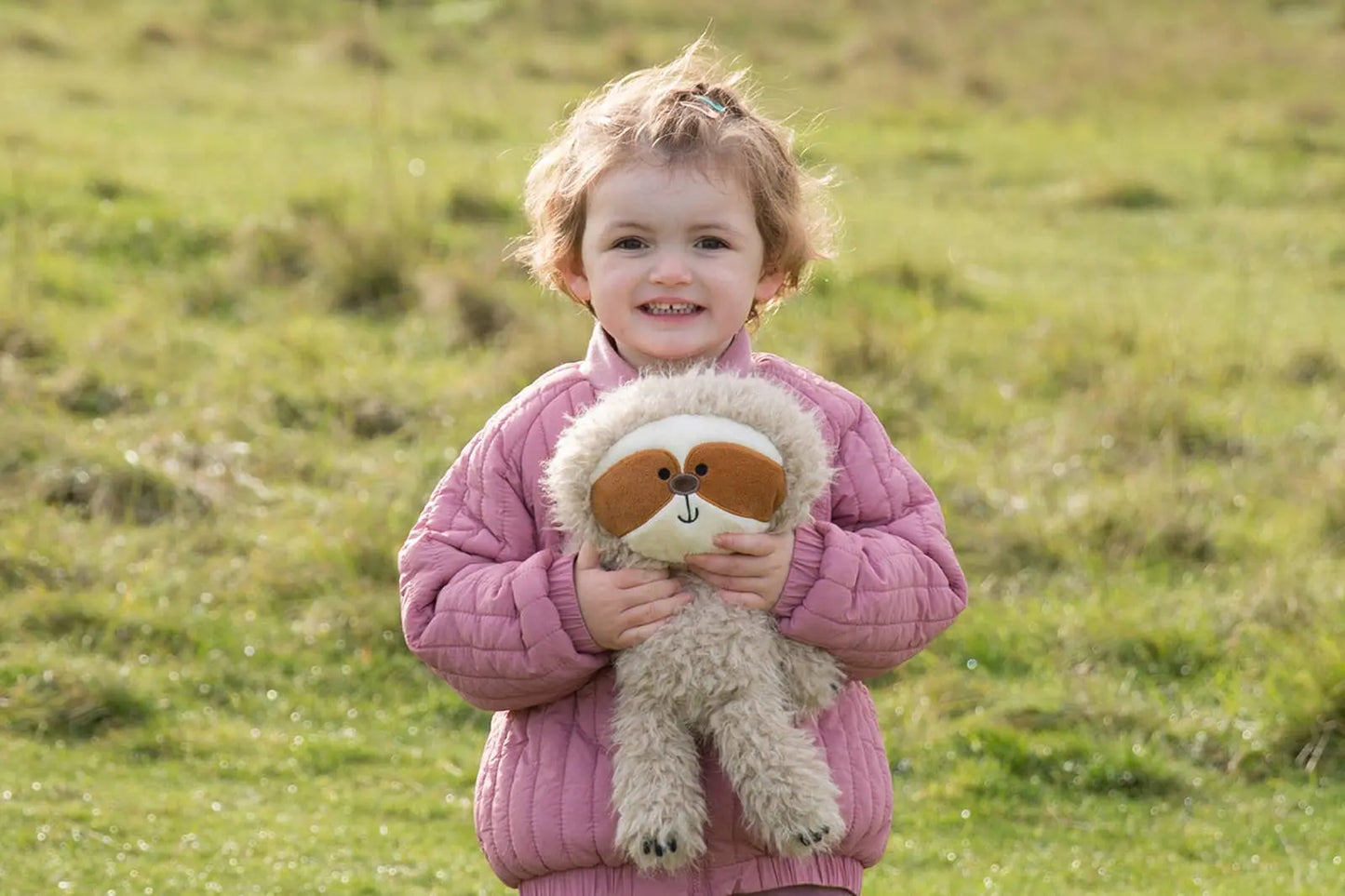 Child holding a stuffed sloth toy in an open field