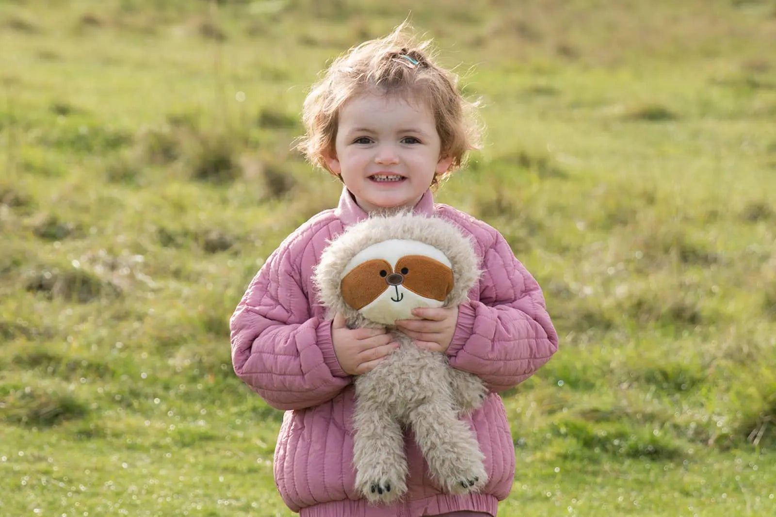 Child holding a stuffed sloth toy in an open field