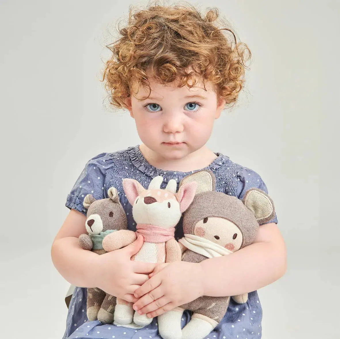 Child holding three plush toys against a plain background