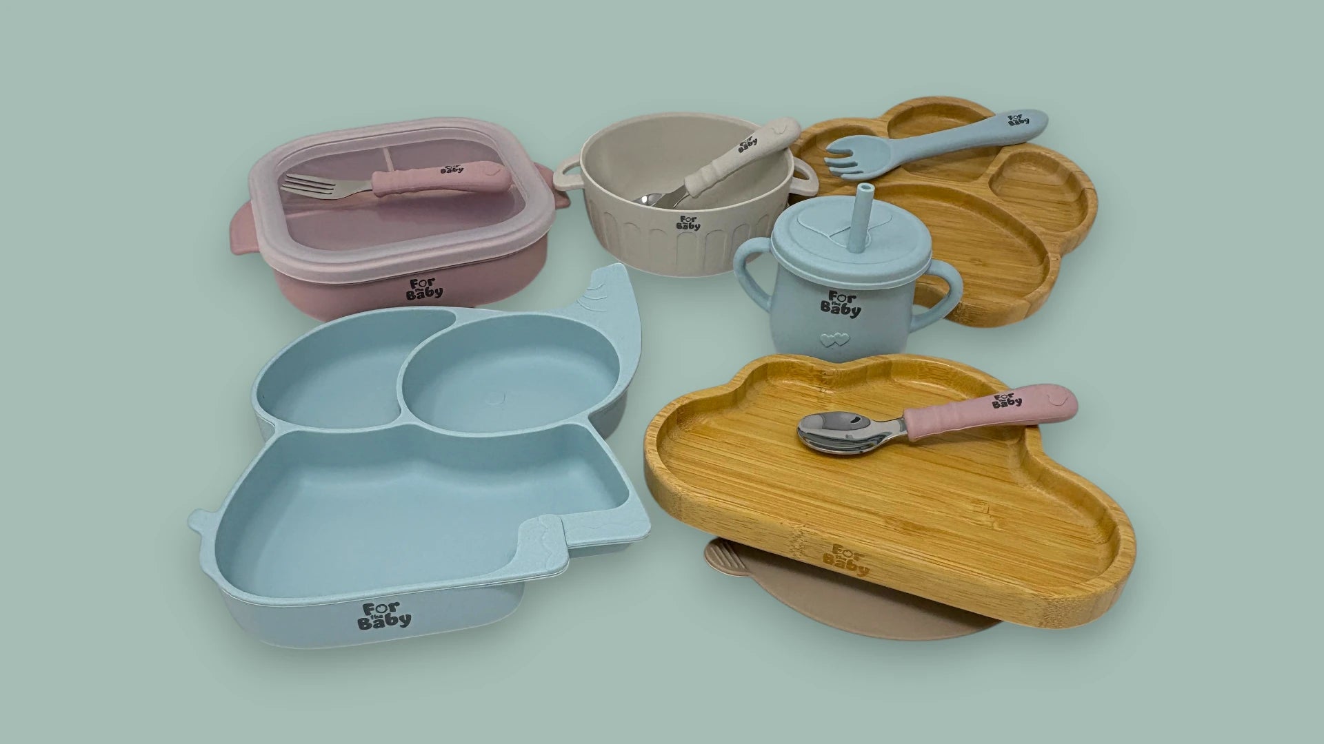 Collection of baby's tableware including plates, cups, and utensils on a light green background