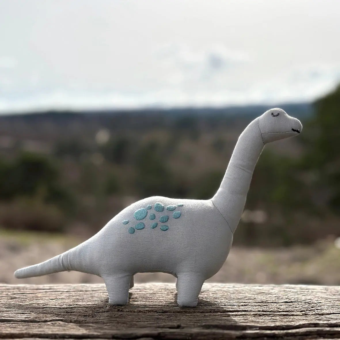 Stuffed dinosaur toy on a wooden log with a blurred natural background