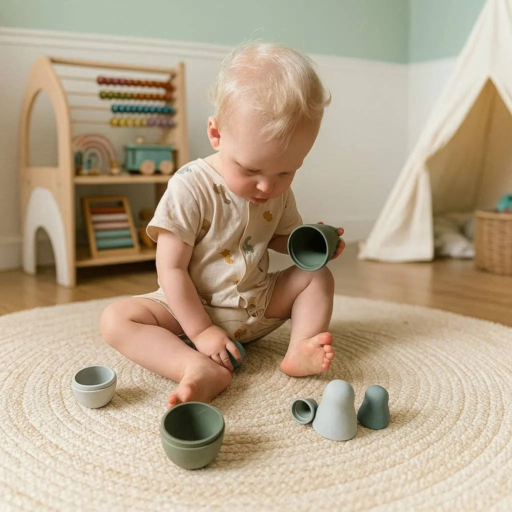 Child playing with silicone nesting dolls on a rug in a room with toys and a playhouse.