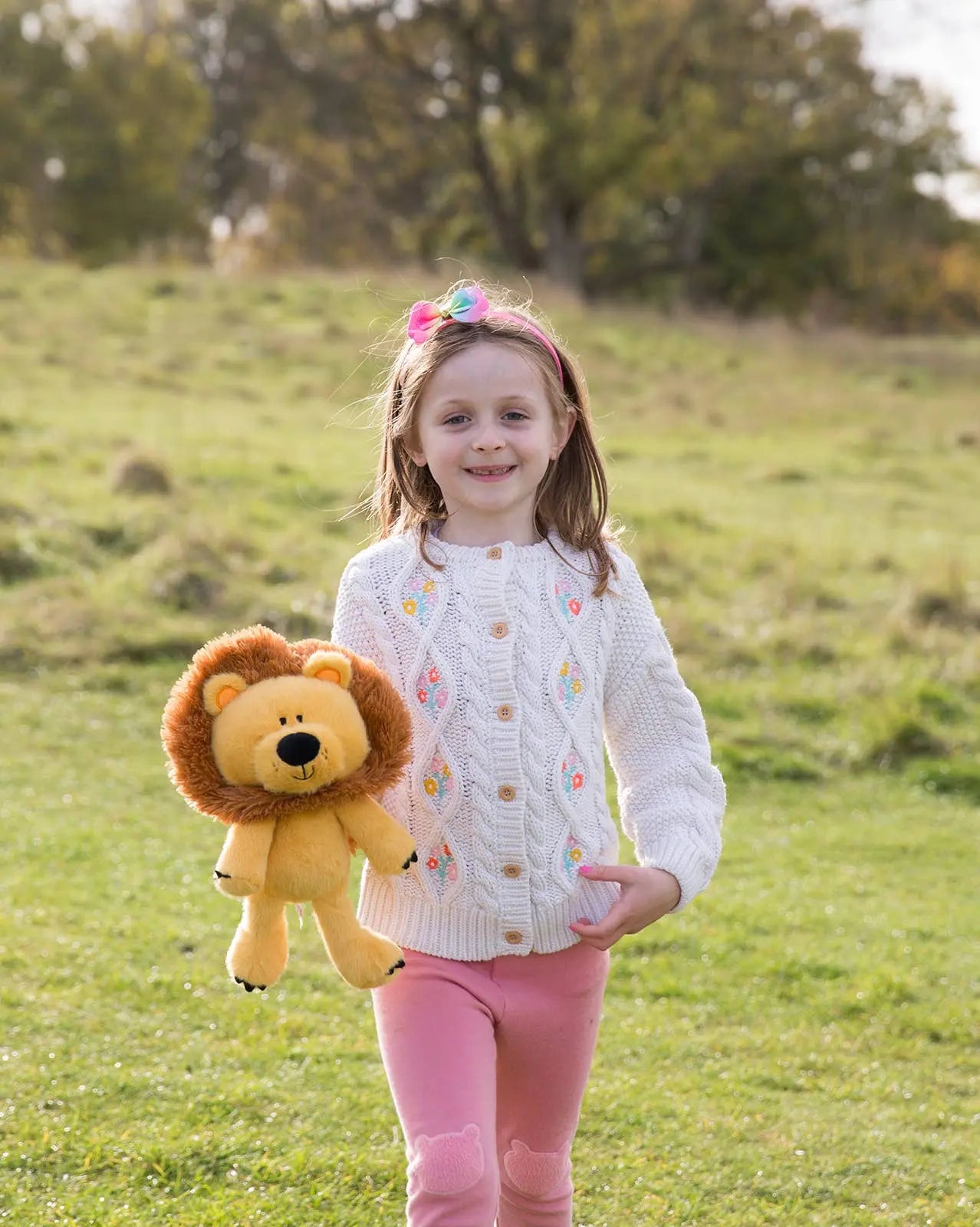 Young girl holding a lion plush toy in a grassy field