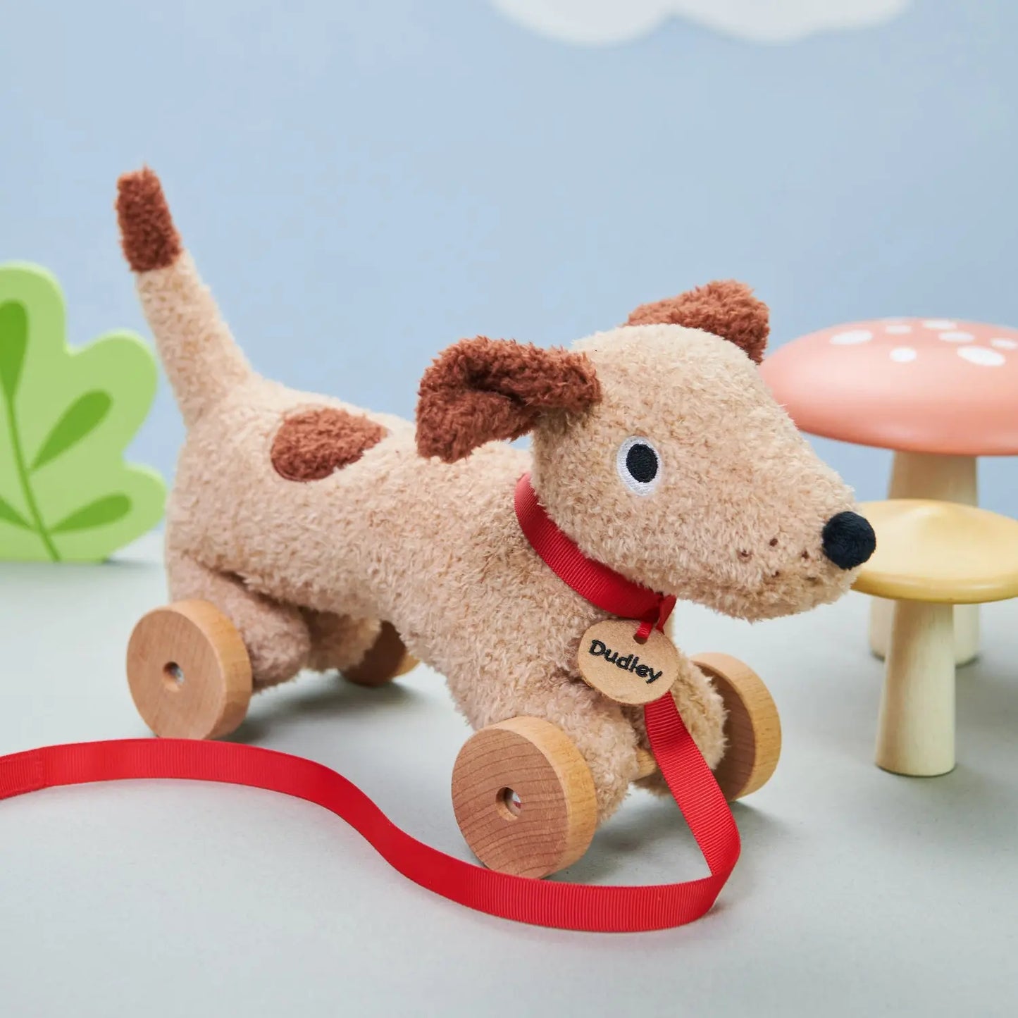 Plush dog toy with wheels and a red ribbon on a light blue background