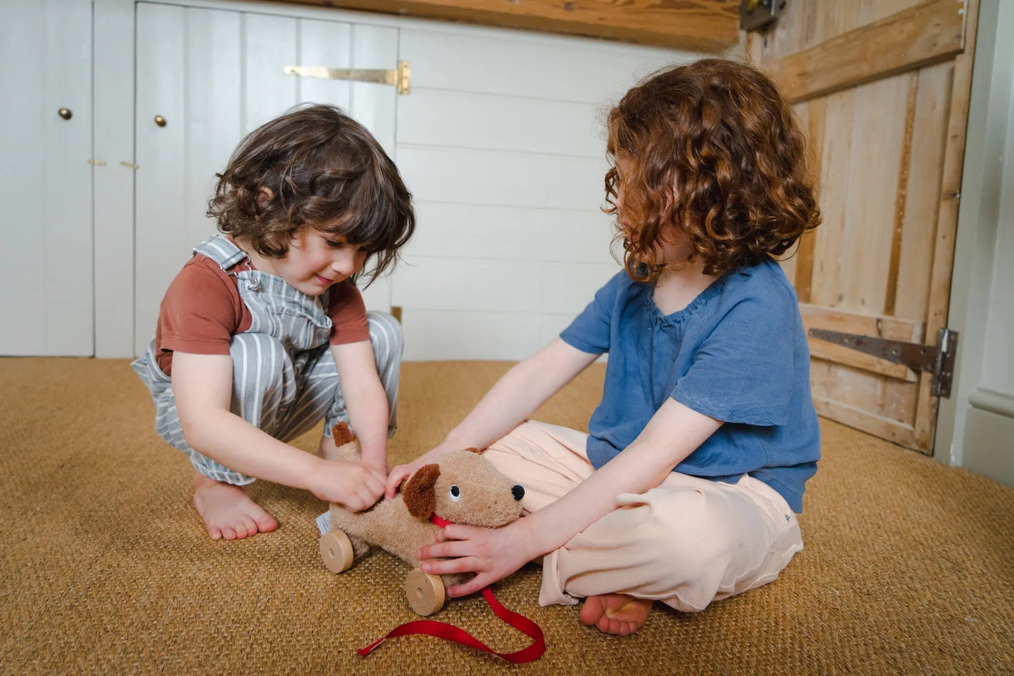 Two children playing with a cute dog toy on a carpeted floor.