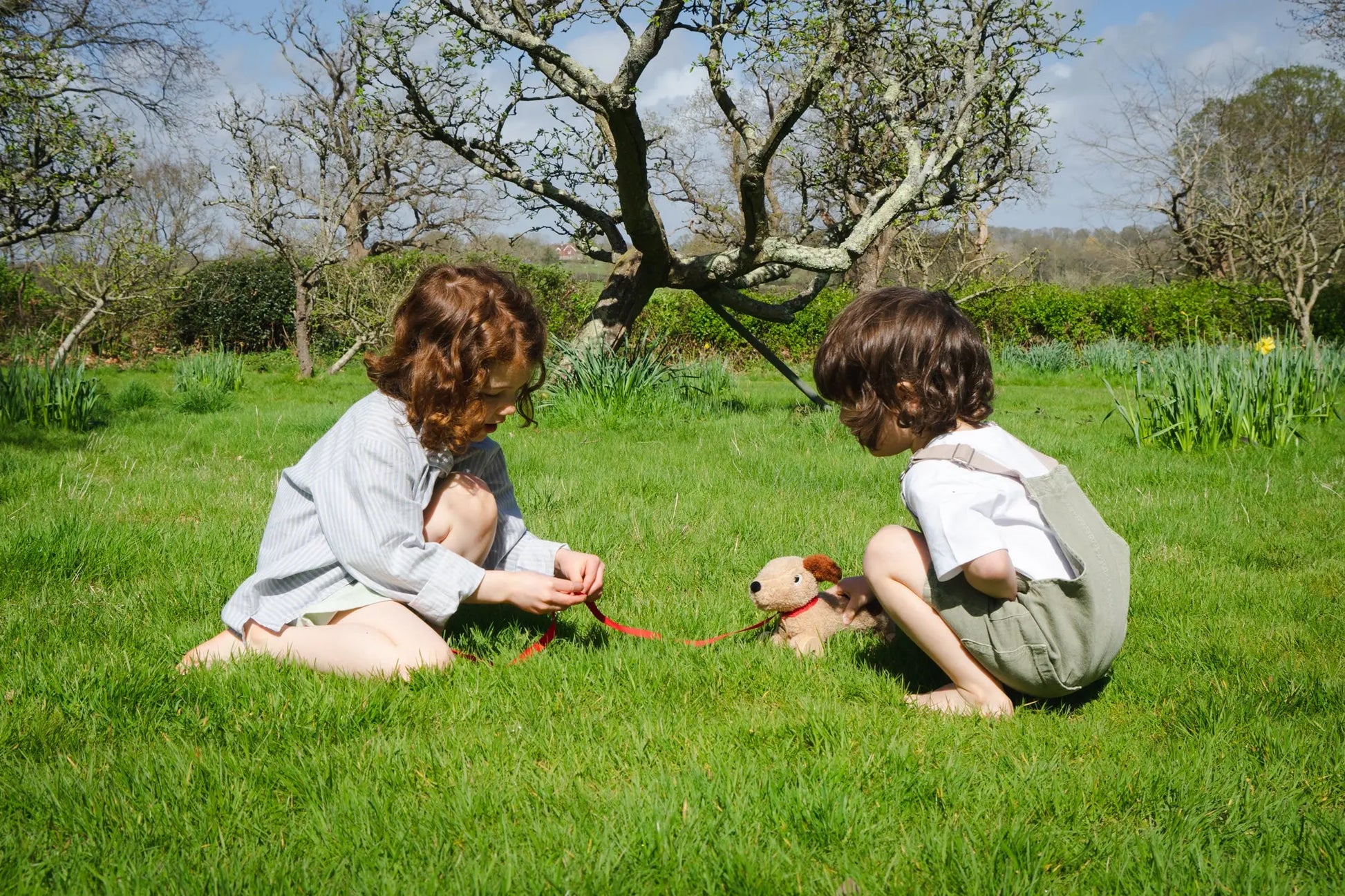 Two children playing with a toy dog on a grassy field.