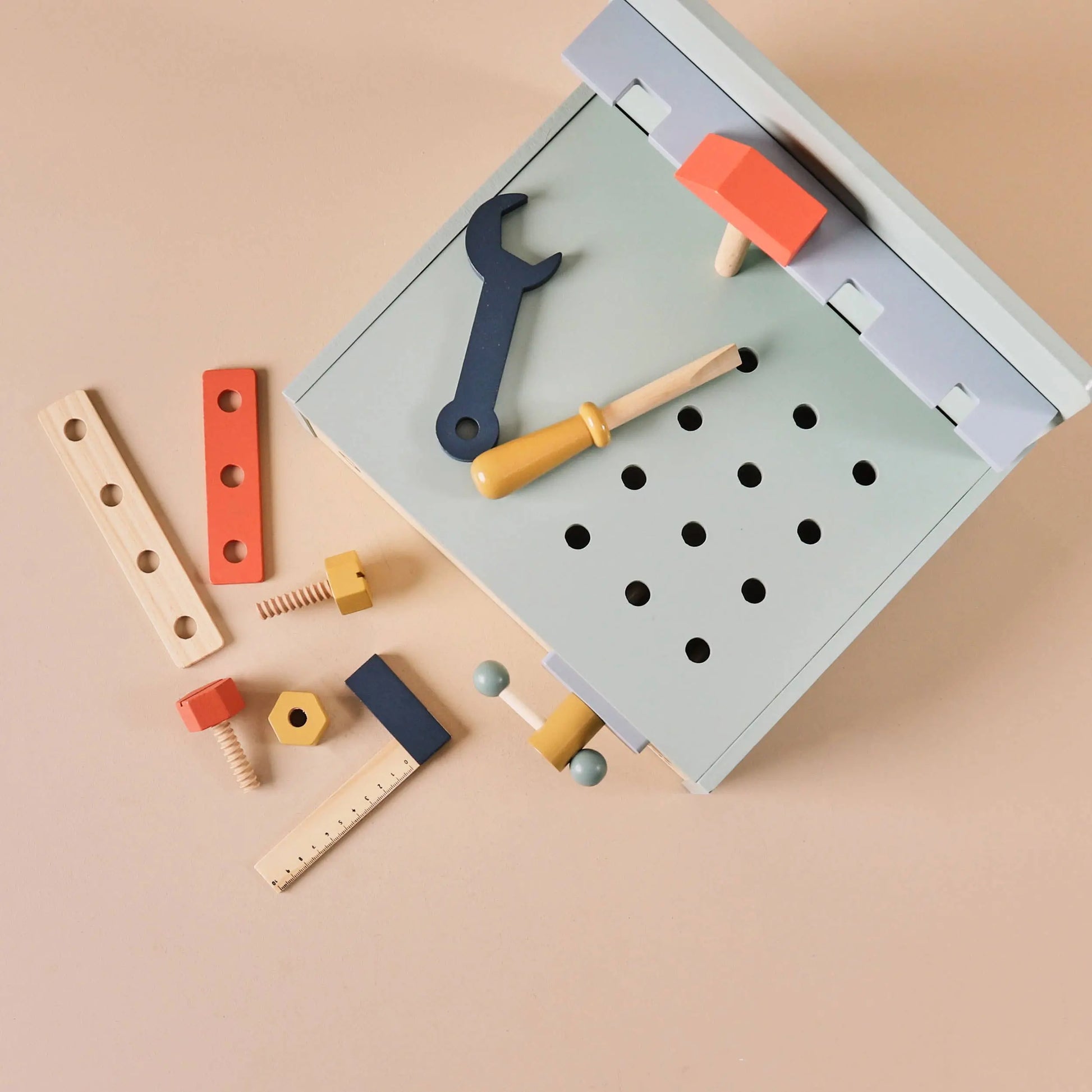 Set of colourful toy tools on a grey pegboard against a beige background
