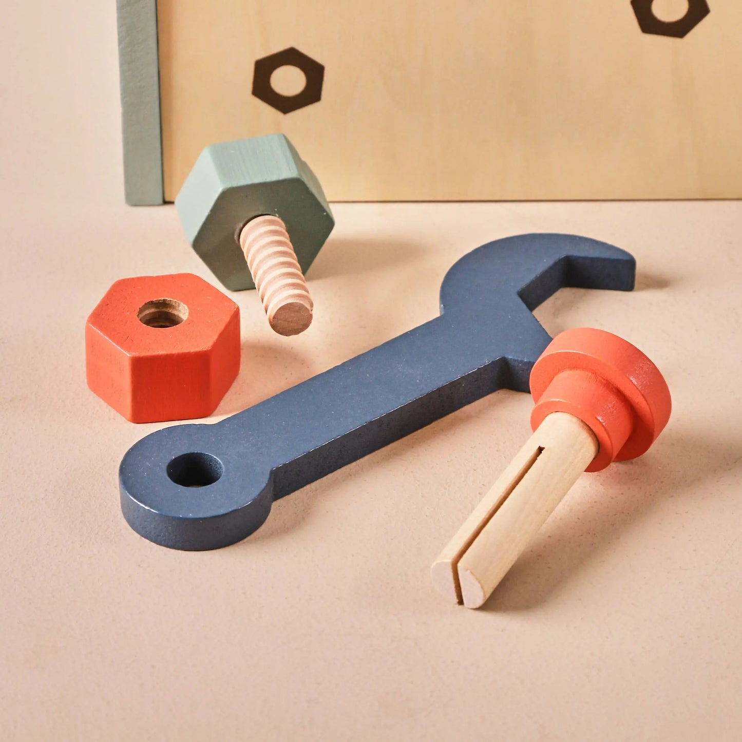 Colourful toy wrench and hexagonal nuts on a beige surface