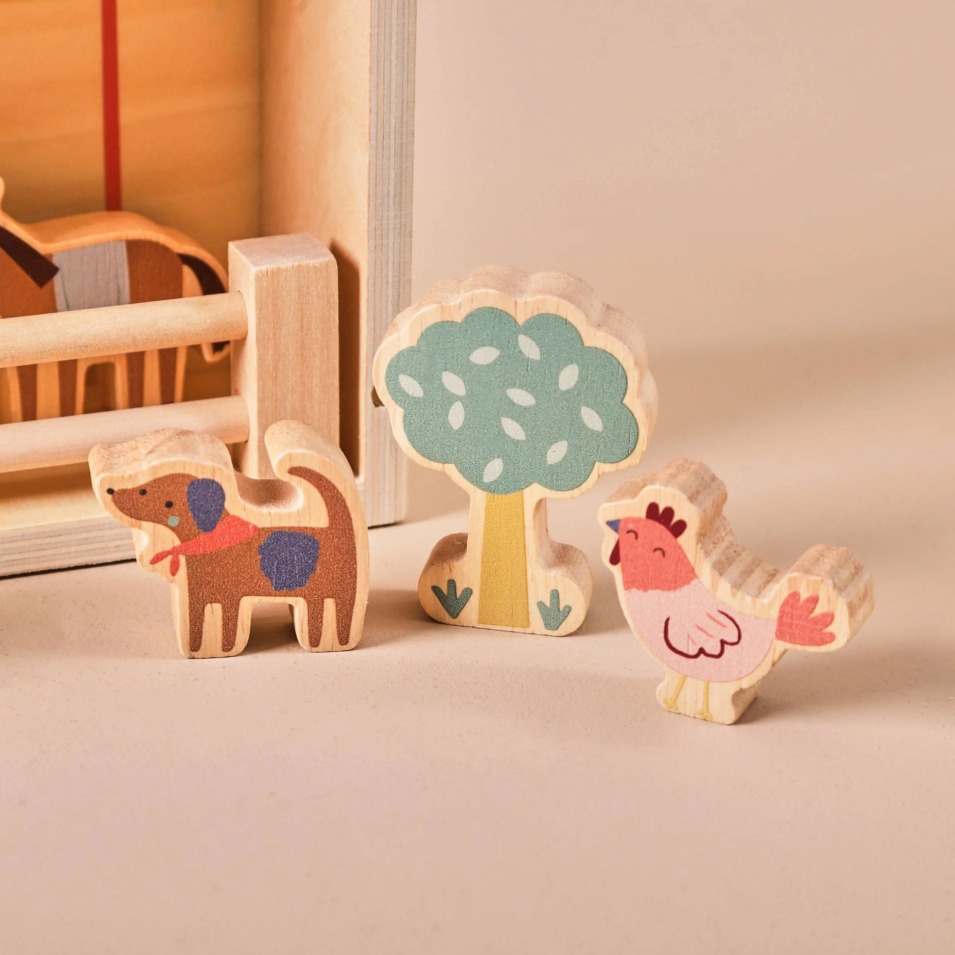 Wooden toys including a dog, tree, and chicken on a beige surface.