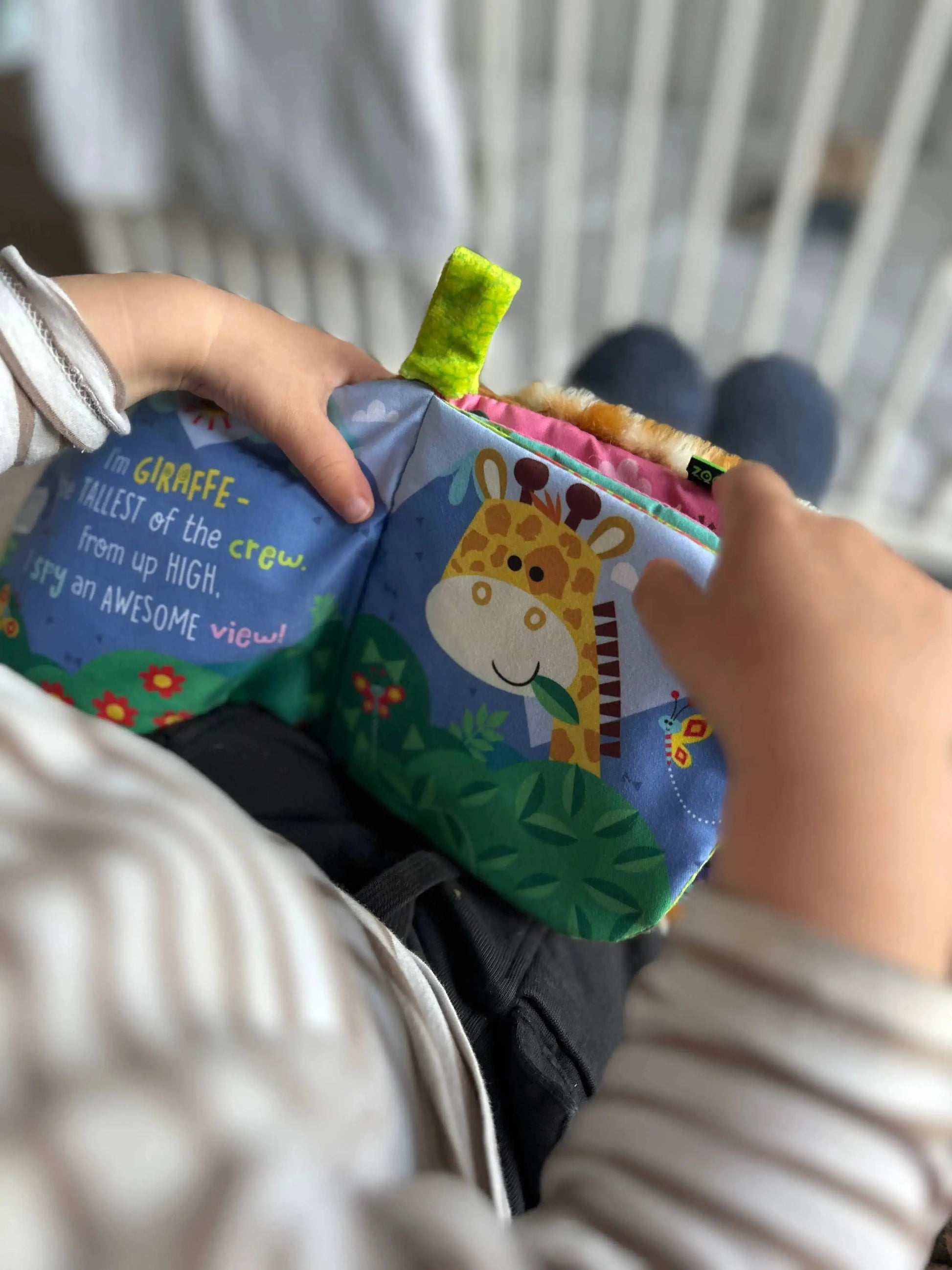 Child holding a soft book with a giraffe illustration and text.