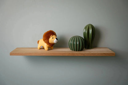 Wooden shelf with a lion figurine and two cacti against a gray wall