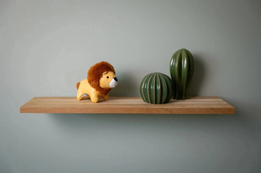 Wooden shelf with a lion figurine and two cacti against a gray wall