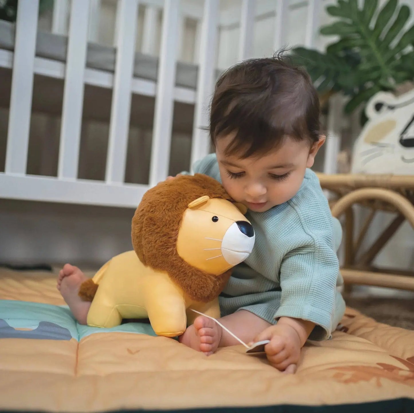 Child playing with a lion toy on a mat in a room with a crib and chair.
