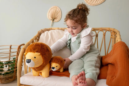 Child sitting on a wicker chair with two lion plush toys