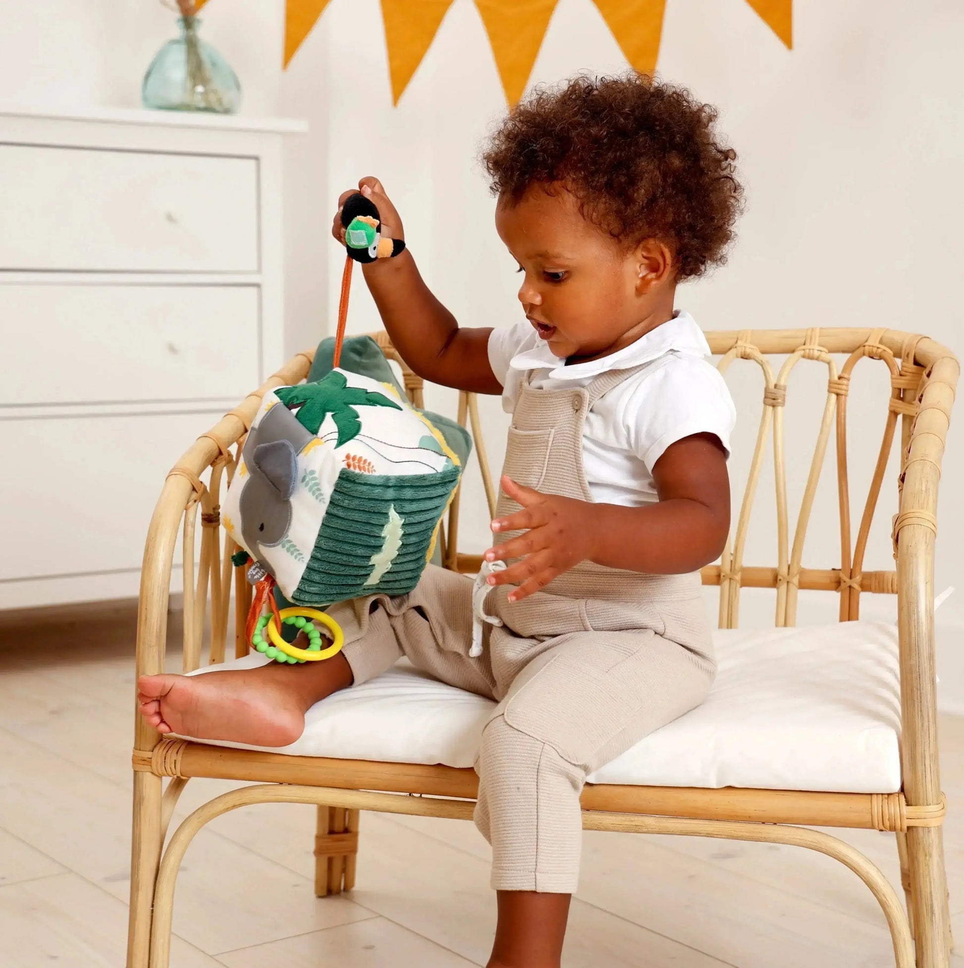 Child sitting on a chair with toys, holding a green toy with a palm tree design.