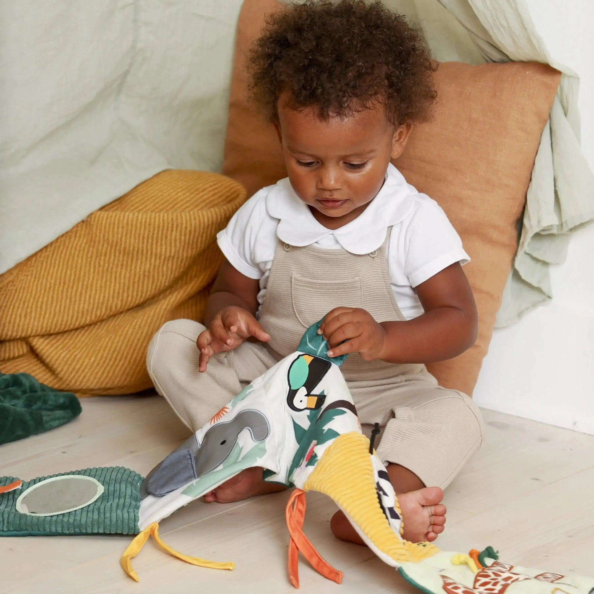 Child playing with a colourful soft book toy on a bed