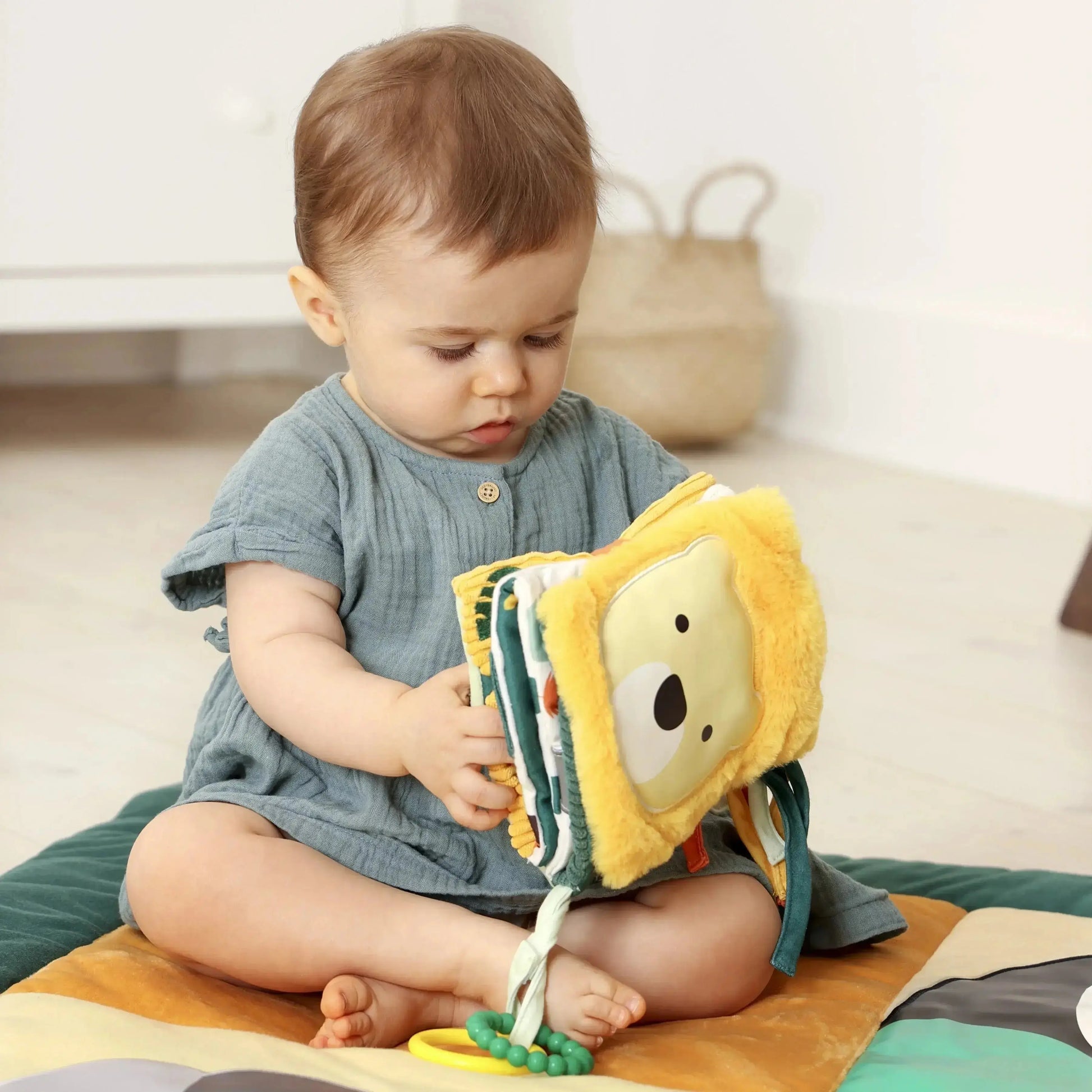Baby playing with a soft toy lion book on a colourful mat