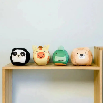 Four colourful animal-shaped balls on a wooden shelf against a light blue wall.