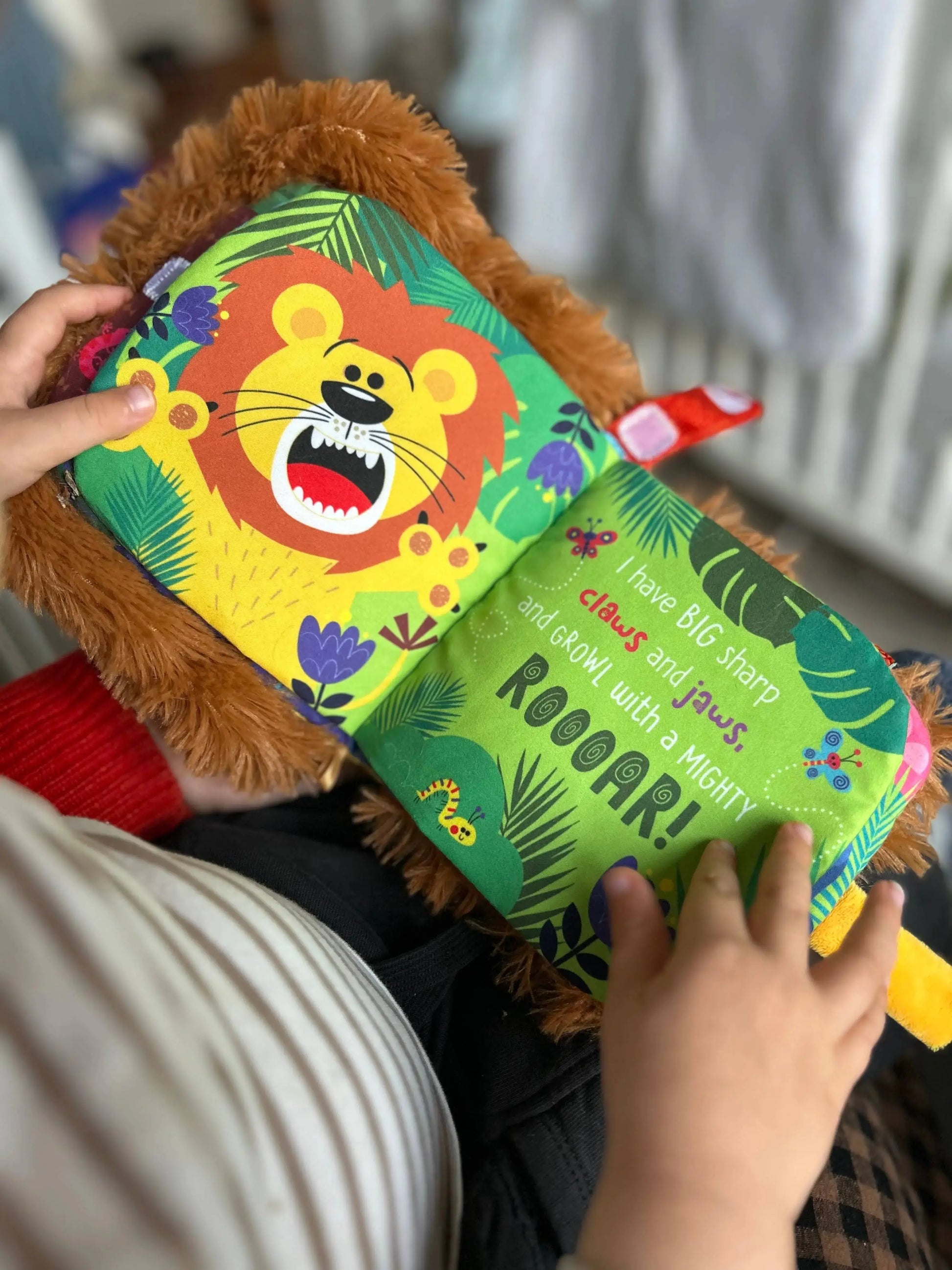 Child holding a colourful children's book with a lion illustration on a soft toy background
