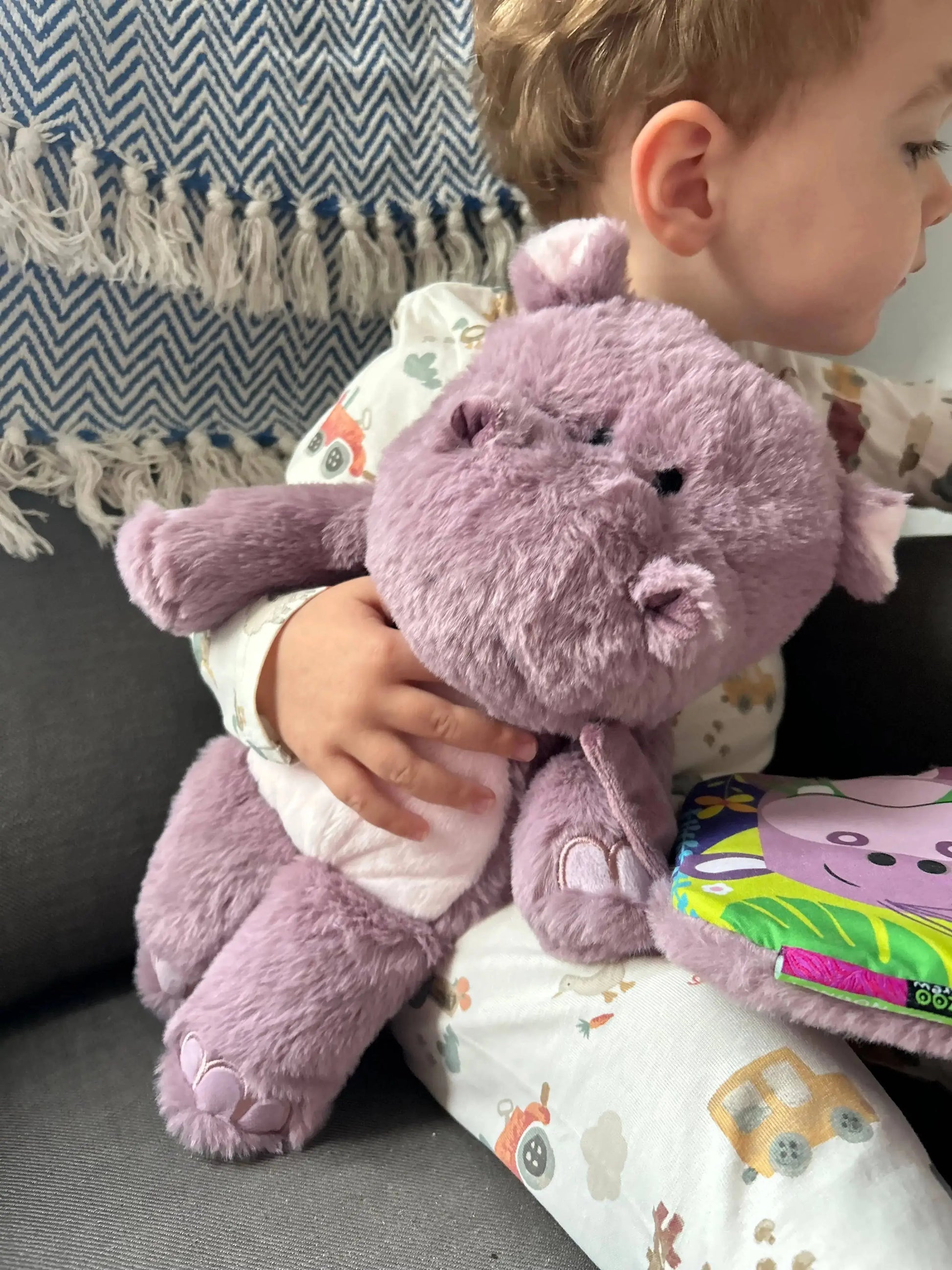 Child holding a purple pygmy hippo with a patterned blanket and couch in the background