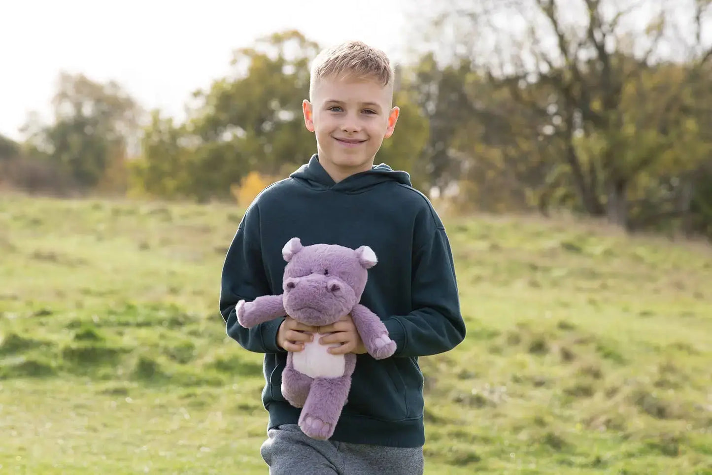 Young boy holding a purple hippo toy in an outdoor setting