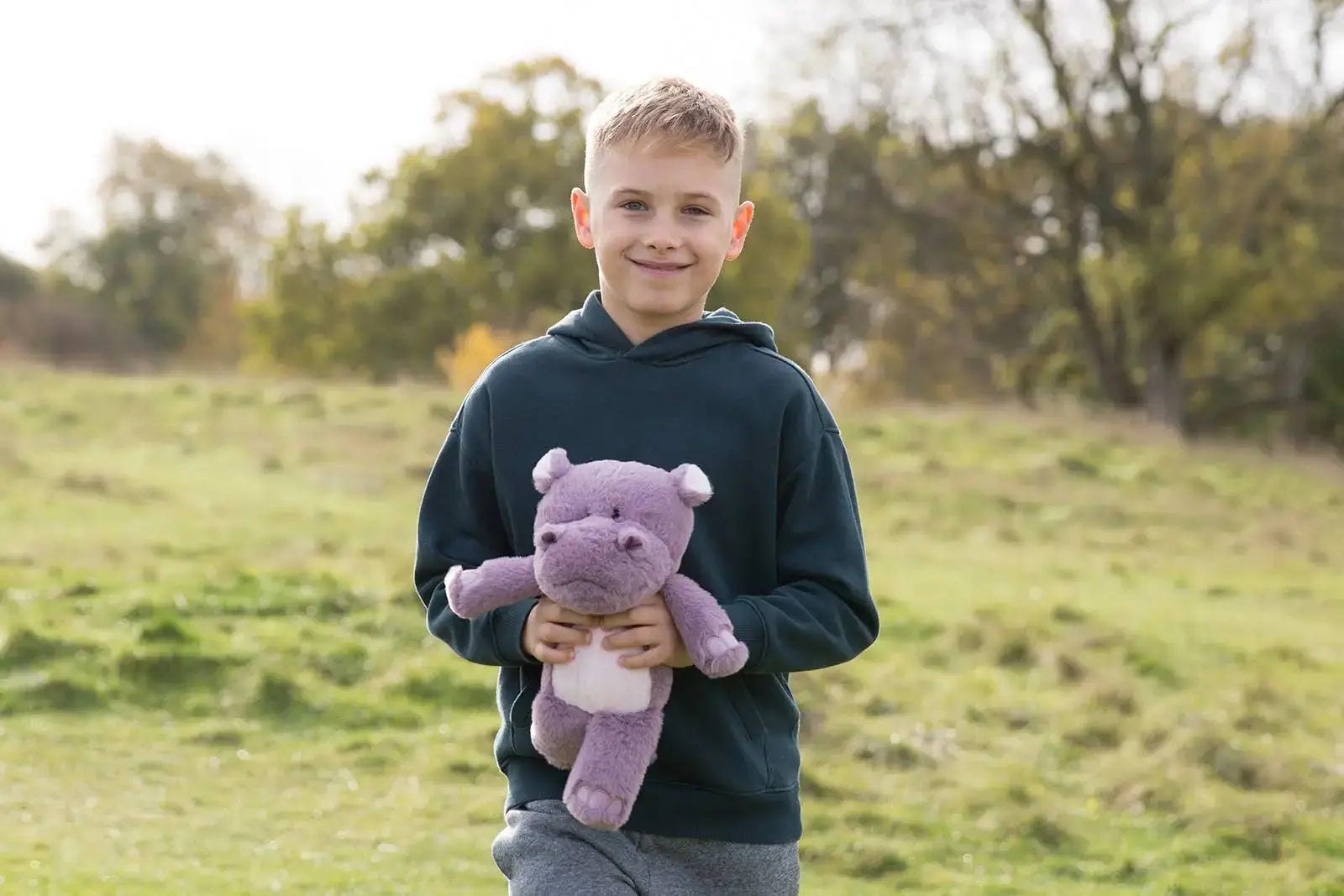 Young boy holding a purple hippo toy in an outdoor setting