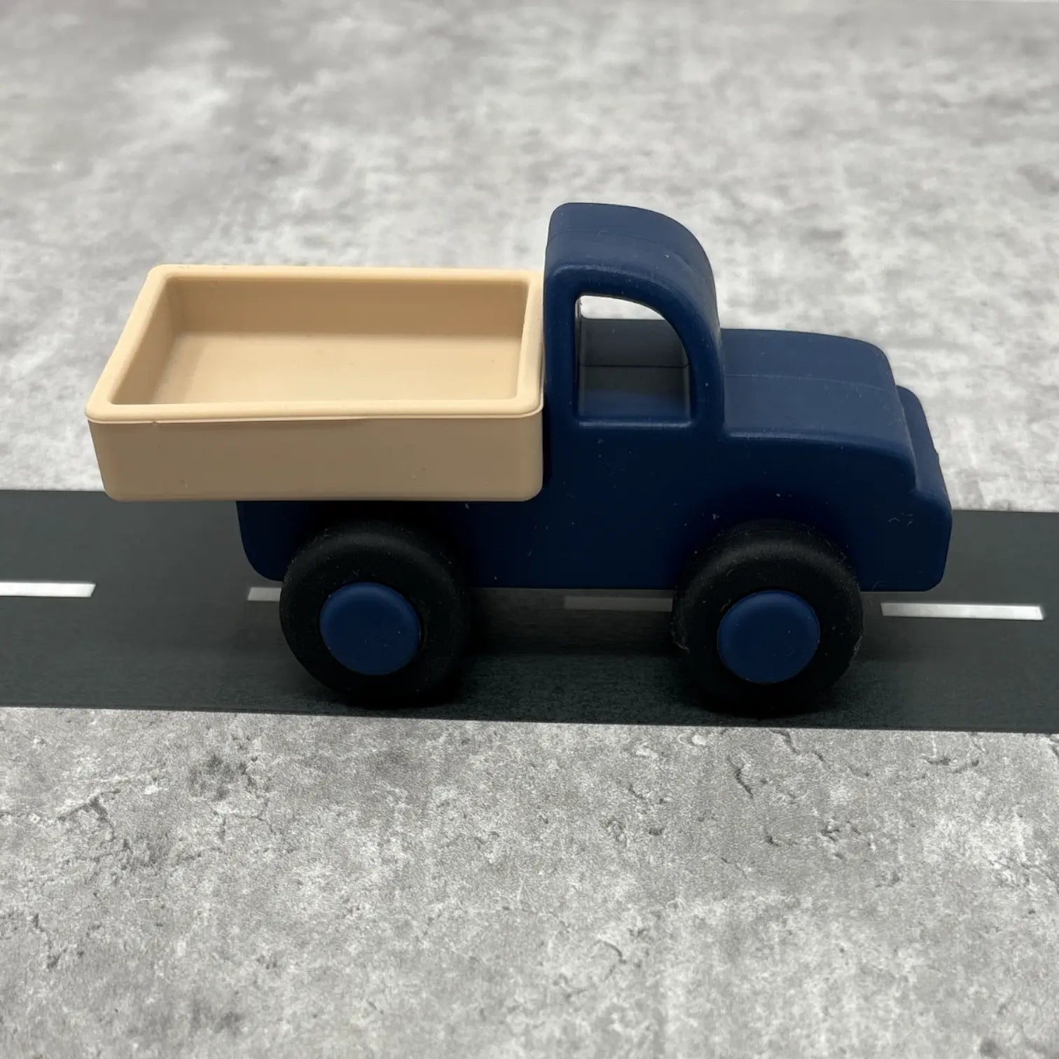 Toy truck with a blue body and beige bed on a grey surface