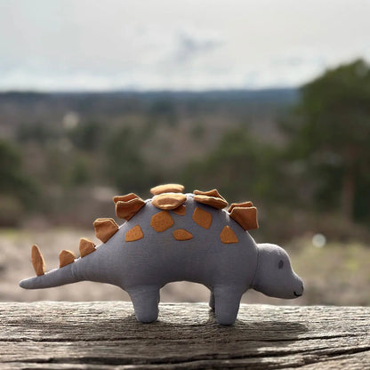 Toy stegosaurus on a wooden surface with a blurred natural background