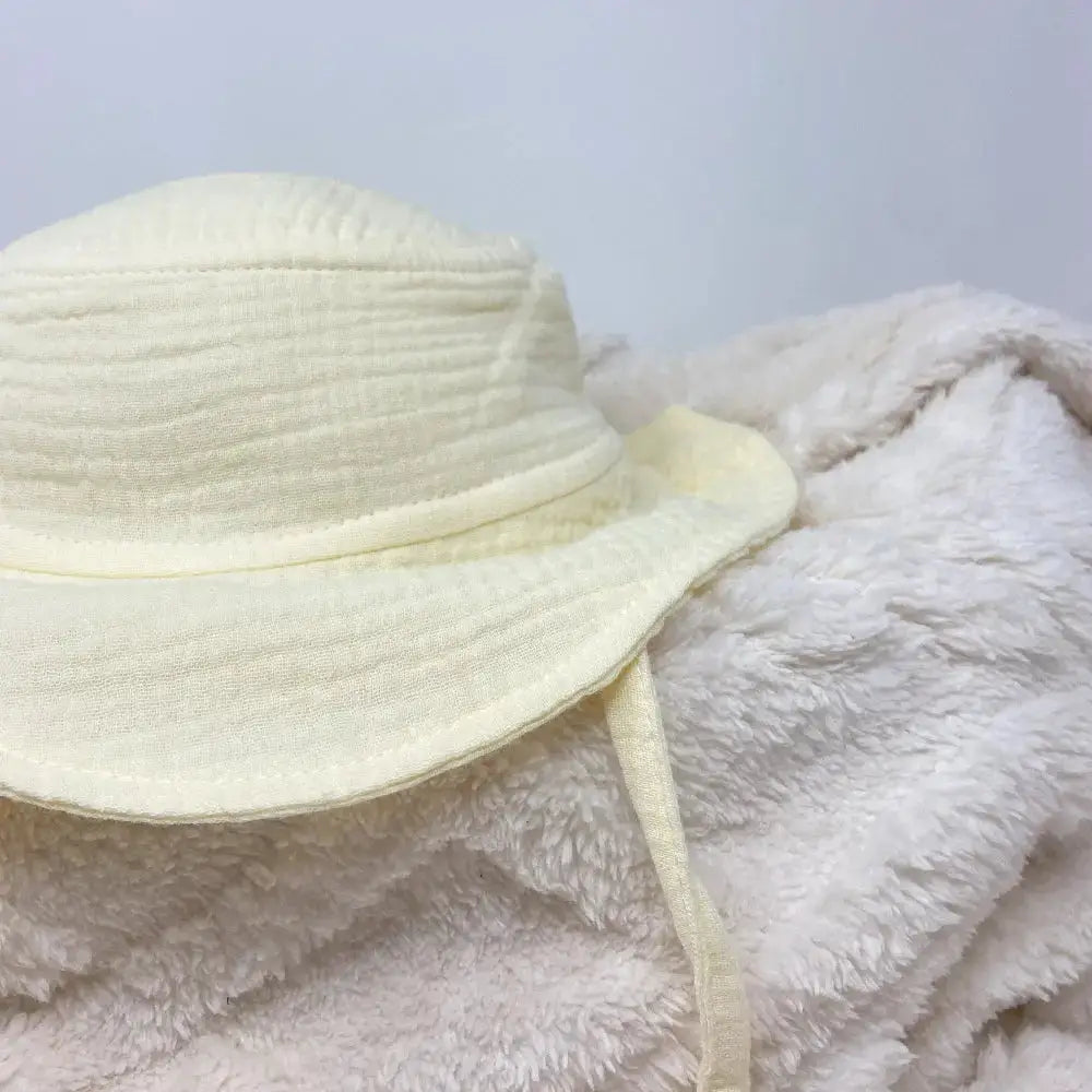 Lemon coloured sun hat on a fluffy white surface with a light grey background
