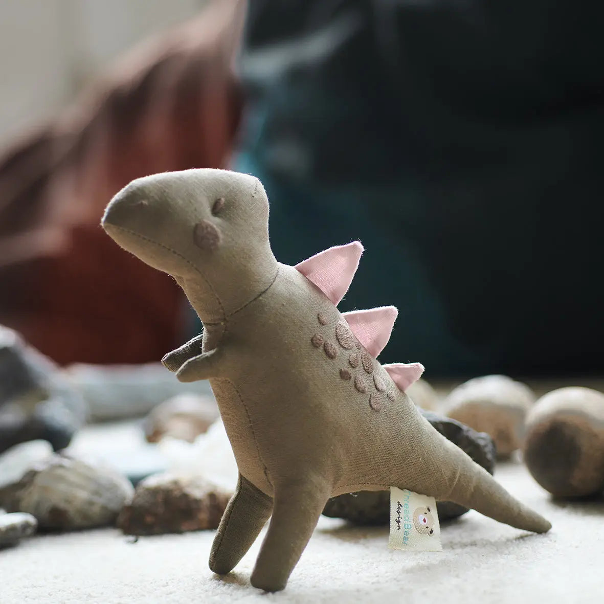 Stuffed dinosaur toy with pink spikes on a surface with rocks