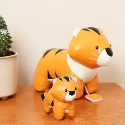 Two tiger figurines on a wooden surface with a plant in the background