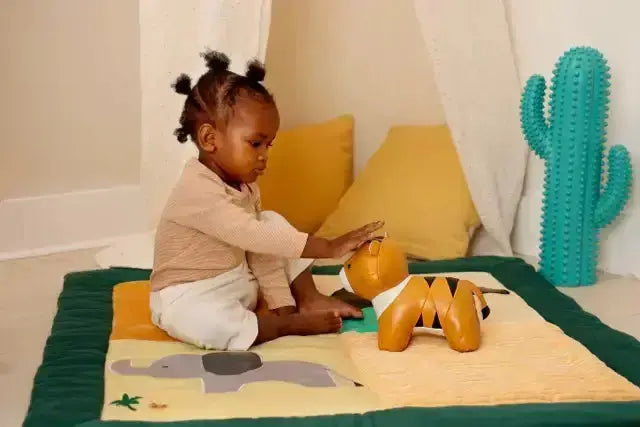 Child playing with a toy on a colourful mat in a room with a cactus decoration.