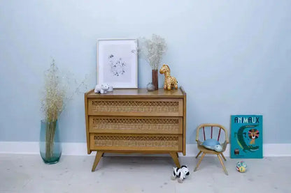 Wooden chest of drawers with decorative items against a light blue wall.