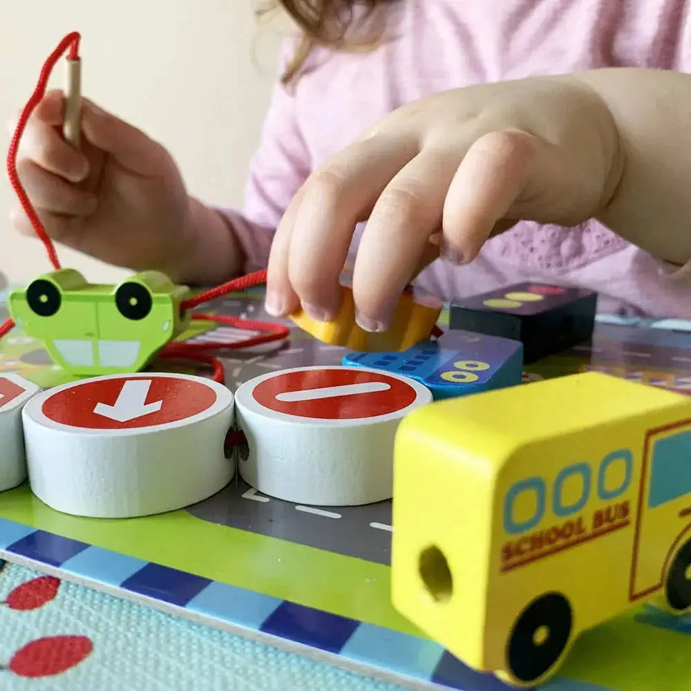 Child playing with educational toys including a school bus and number blocks on a colourful mat.