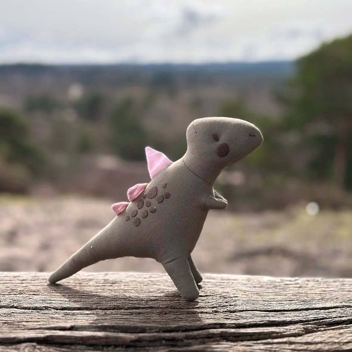Small dinosaur figurine with pink spikes on a wooden surface with a blurred natural background